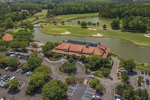 An aerial view of a golf course with a building surrounded by parking and trees.