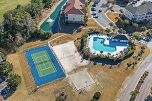 An aerial view of a residential area with a swimming pool, tennis court, and a large house.