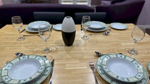 Mesa de jantar posta com pratos, copos e talheres, com um vaso decorativo no centro.