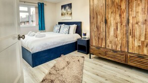 A bedroom with a bed, a wooden wardrobe, a nightstand, a painting, and a window with curtains.