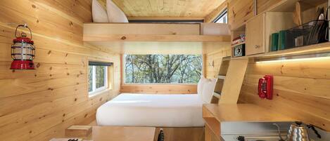 A compact cabin with a bunk bed, a small kitchenette, and a window overlooking trees.