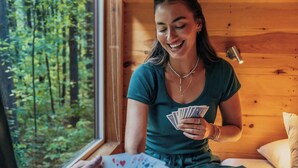 A person sitting on a wooden floor inside a cabin, holding playing cards. - Postcard Cabins Western Catskills, Outdoor Collection by Marriott Bonvoy (Roscoe)