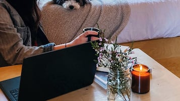 Una persona trabajando en un ordenador portátil sobre una mesa de madera, con una vela y un tarro de flores.