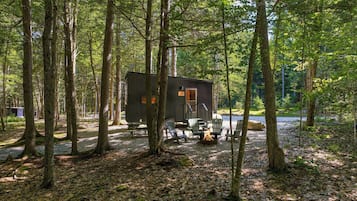 A cabin in a forest with a picnic table and chairs.
