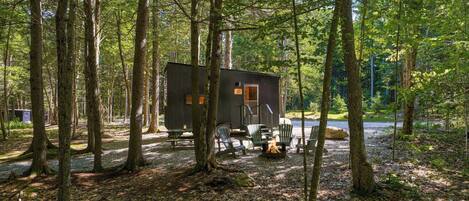 Eine Hütte im Wald mit einem Picknicktisch und Stühlen.