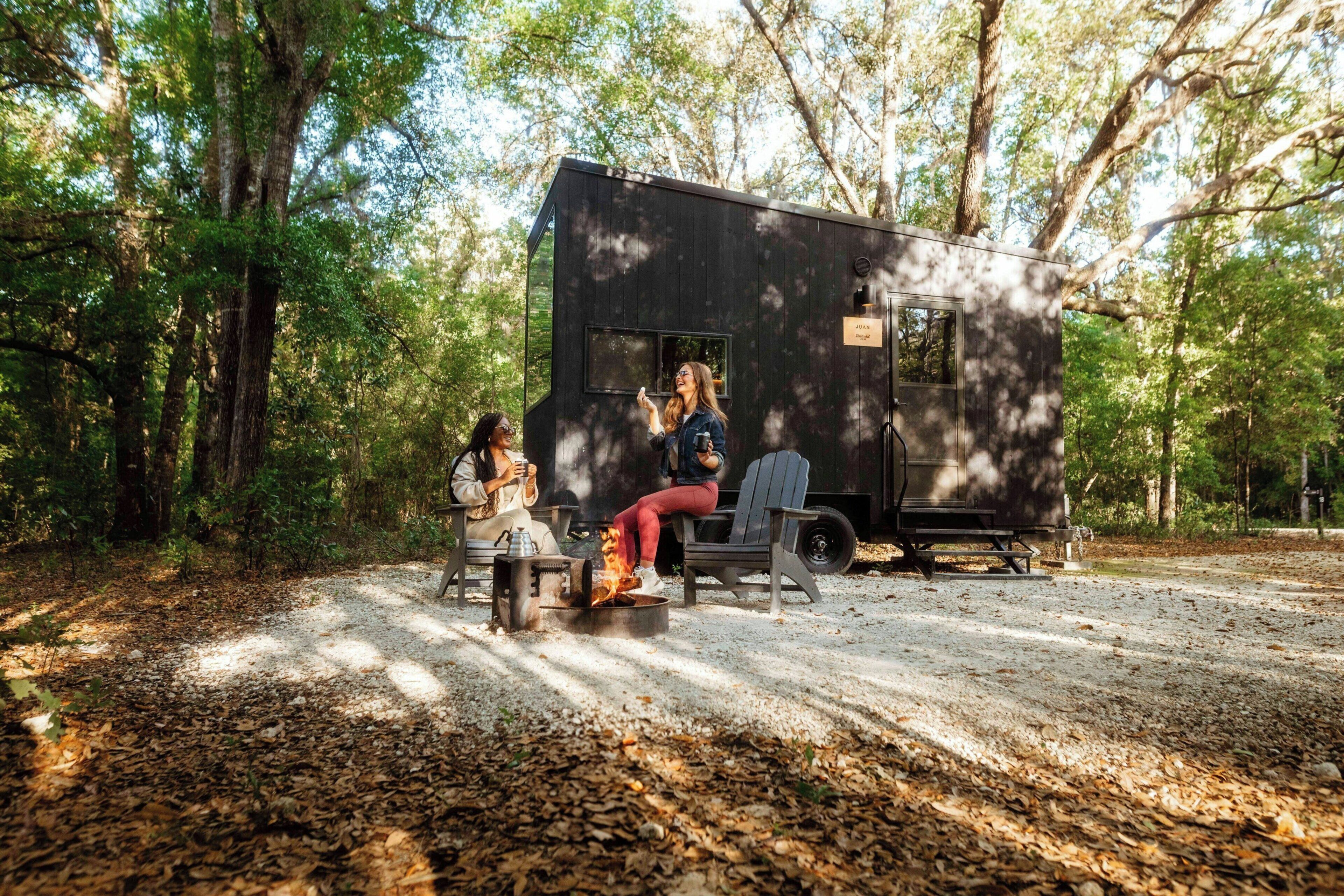 Une petite cabane avec un foyer et une table, entourée d’arbres.