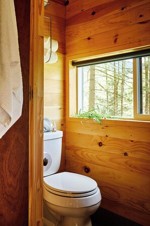 Un baño rústico con cabaña, que incluye un inodoro, una ventana y una toalla colgada en la pared.