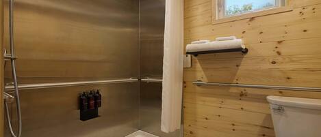A wooden cabin bathroom with a shower, toilet, and a window.