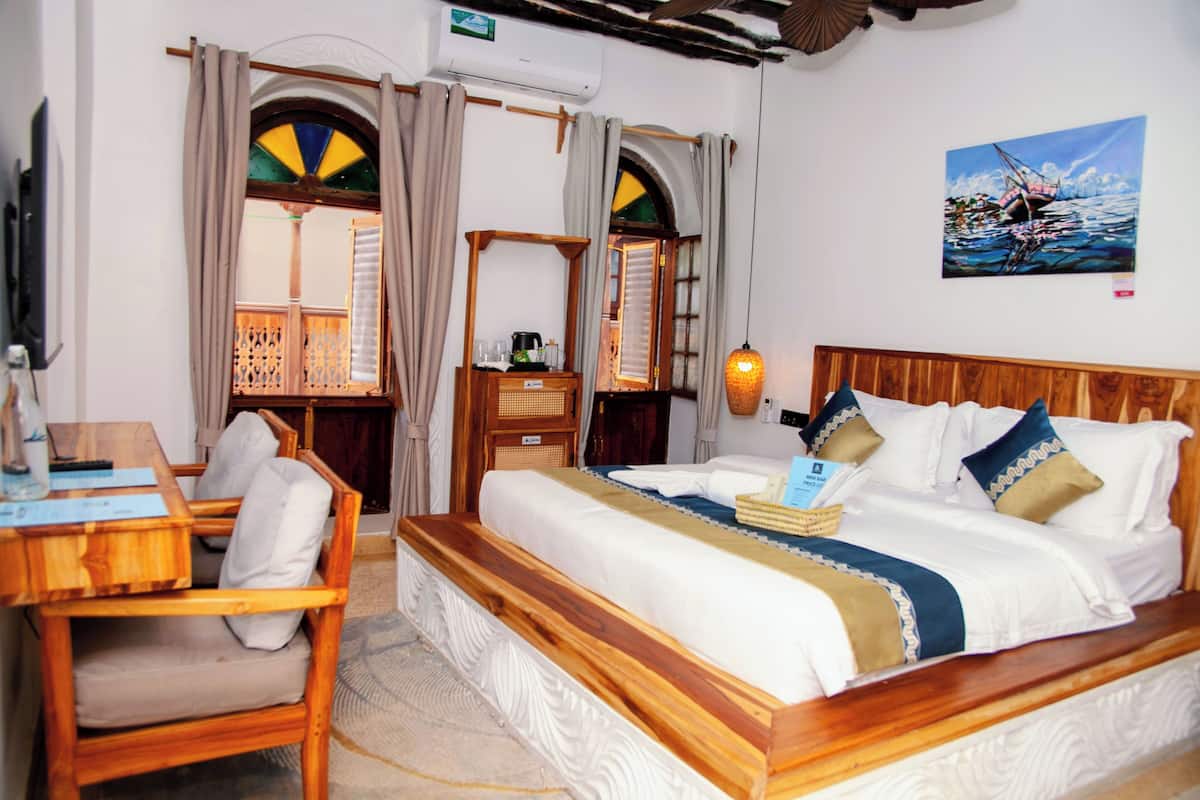 Una habitació amb un llit, un escriptori i una cadira. Hi ha un quadre a la paret i una finestra amb cortines.