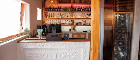 Zona de bar con mostrador de madera, estantes con botellas, máquina de café y enfriador de vino.