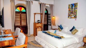 Habitación de hotel con cama, escritorio y silla. Se ve una ventana con un diseño de vitral.