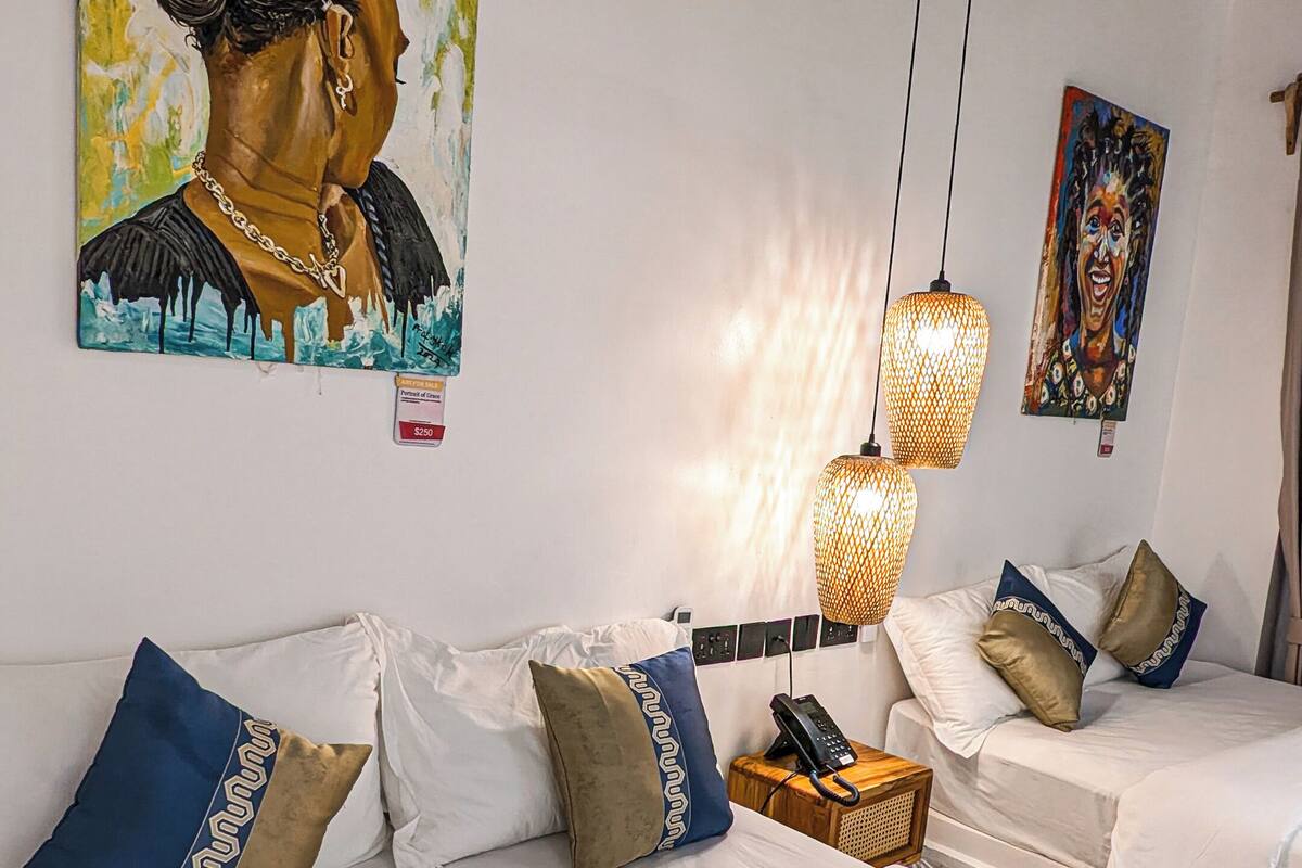 Habitació d'hotel moderna amb un sofà blanc, coixins decoratius, un quadre i un telèfon sobre una taula auxiliar de fusta.