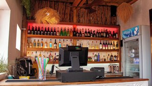 Zona de bar con techo de madera, luces colgantes y una variedad de botellas en estanterías.