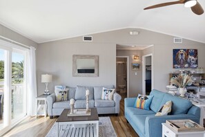 A spacious living room with a high ceiling, a ceiling fan, and a view through a large window.