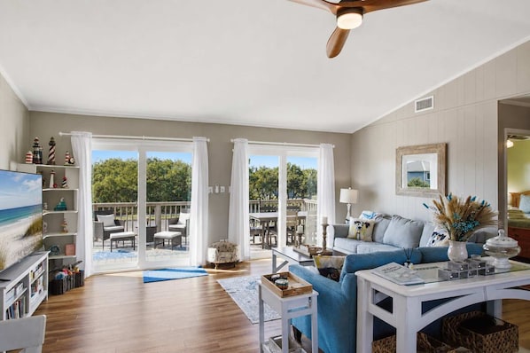 A spacious living room with a large sliding glass door leading to an outdoor patio, a ceiling fan, and a cozy seating area with a sofa and armchairs.