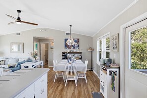 A spacious living area with a dining table, white furniture, and a kitchen in the background.