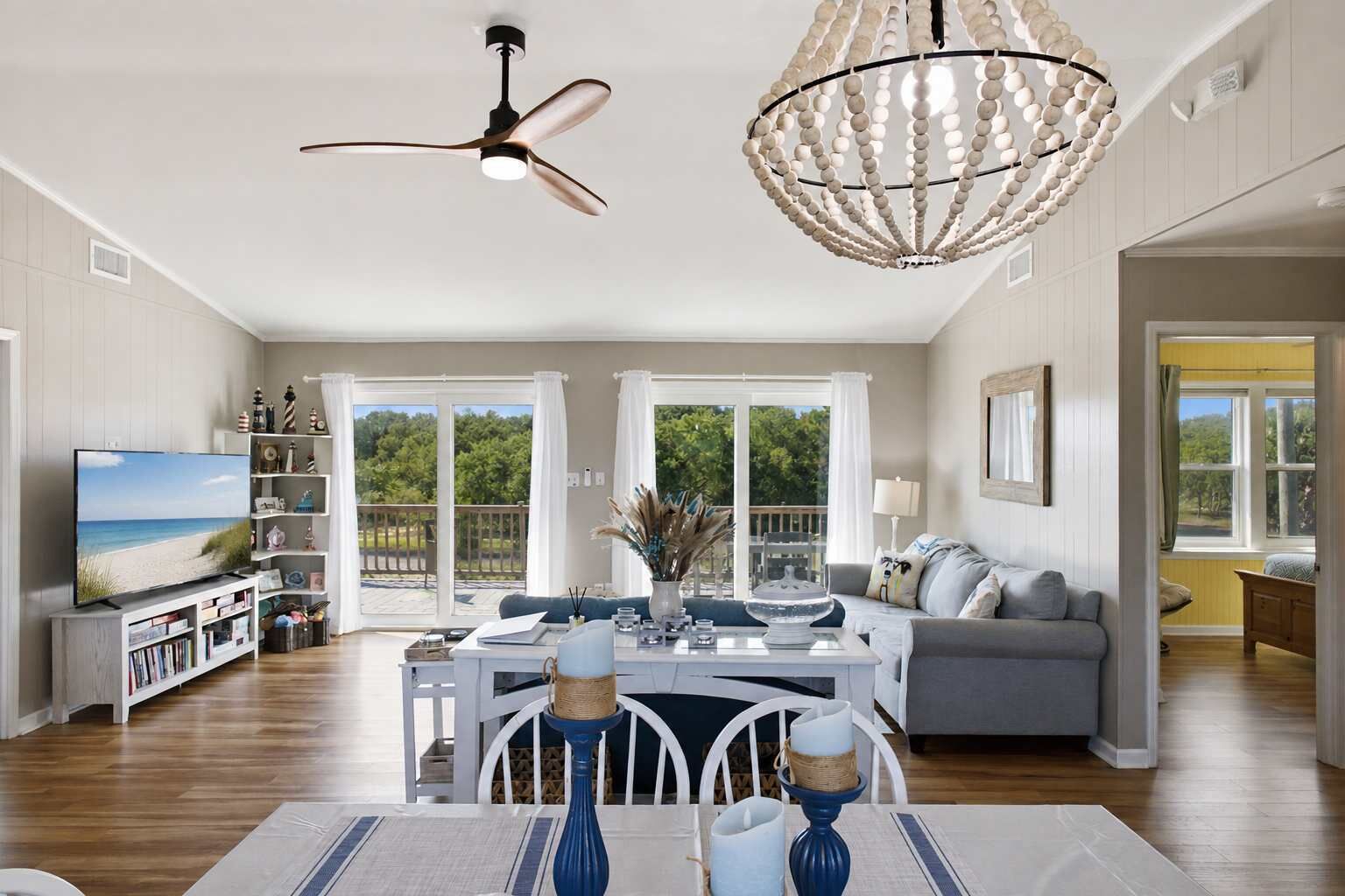 A spacious living room with a television, a dining area with a table and chairs, a ceiling fan, and a decorative chandelier.