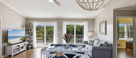 A spacious living room with a television, a dining area with a table and chairs, a ceiling fan, and a decorative chandelier.