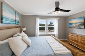 A bedroom with a bed, a dresser, a ceiling fan, and a window with curtains.