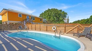 Una piscina con cubierta de madera, un flotador salvavidas y un edificio amarillo al fondo.