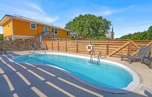 A swimming pool with a wooden deck, a lifebuoy, and a yellow building in the background. - Honey Hole on St George Island Pet Friendly Private Pool (Heated for a fee) West Gulf beaches (Saint George Island)