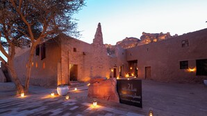 A courtyard with stone buildings, a large rock, and lanterns. - Dar Tantora The House Hotel (Al-'Ula)
