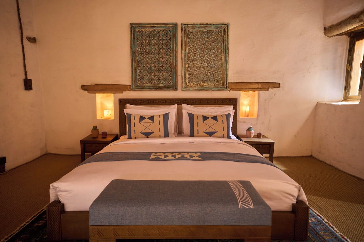 Quarto bem arrumado com uma cama grande, duas luminárias na parede e dois painéis decorativos sobre a cama.