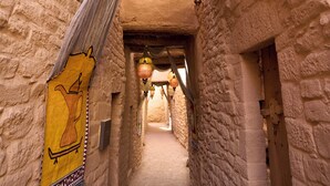 A narrow, stone-walled corridor with hanging lanterns and a yellow tapestry on the left wall. - Dar Tantora The House Hotel (Al-'Ula)