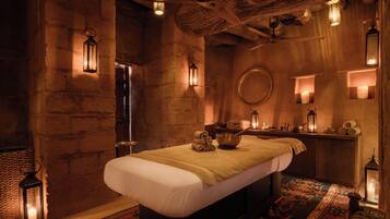 Cozy retreat with a large bed, wooden bench, and small table, set amidst exposed stone walls and a rustic ceiling.