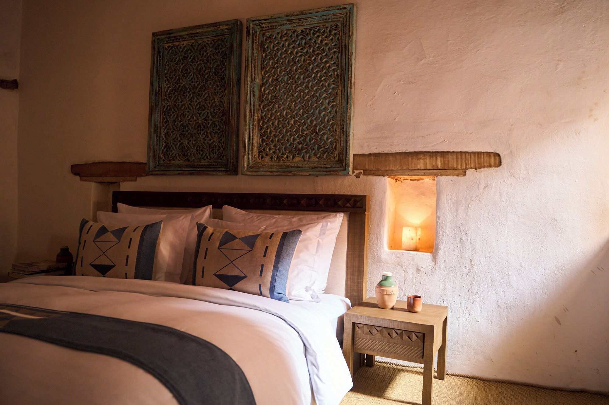 A bedroom with a bed, pillows, a nightstand, a lamp, and two wall-mounted decorative panels.