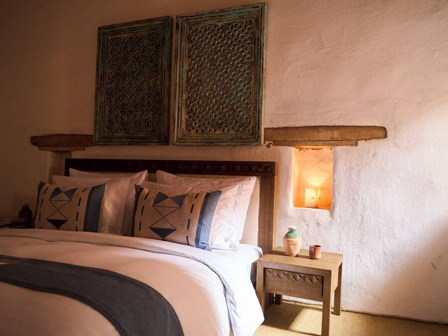 A bedroom with a bed, pillows, a nightstand, a lamp, and two wall-mounted decorative panels.