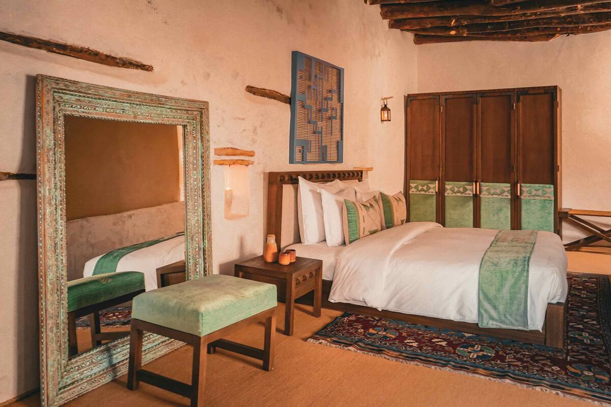 Quarto tradicional com cama, um banco, um espelho e guarda-roupa de madeira.