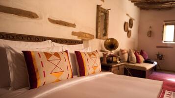 A bed with patterned pillows, a wooden headboard, and a rustic wall with a mirror and decorative items.