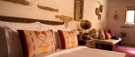A bed with patterned pillows, a wooden headboard, and a rustic wall with a mirror and decorative items.
