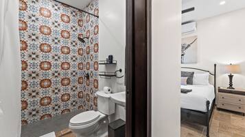 Ein Badezimmer mit Dusche, Toilette und Waschbecken sowie ein Schlafzimmer mit Bett und Nachttisch.