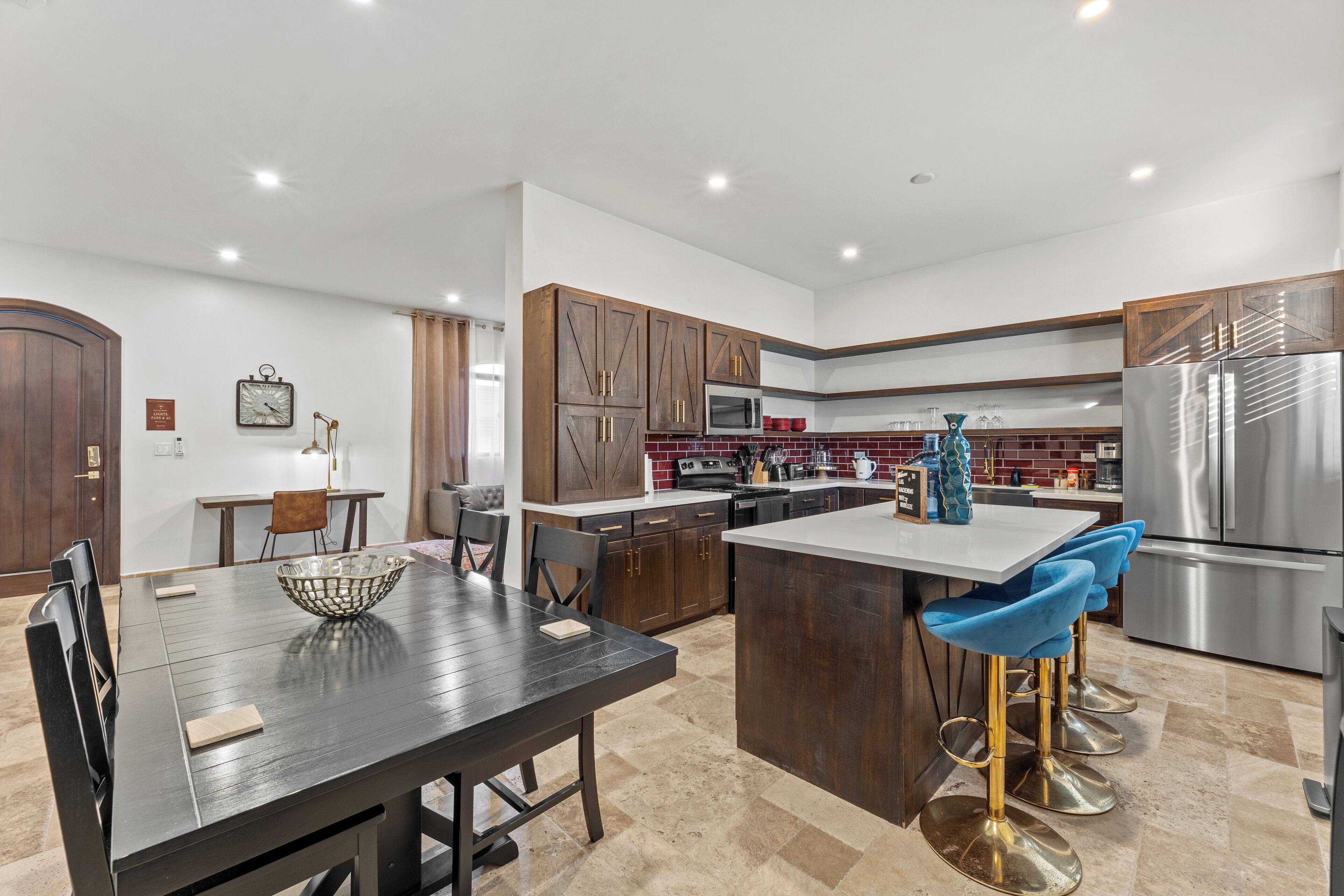A modern kitchen with dark wooden cabinets, stainless steel appliances, and a central island with blue bar stools.