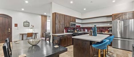 A modern kitchen with dark wooden cabinets, stainless steel appliances, and a central island with blue bar stools.
