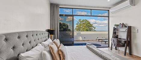 A modern bedroom with a large bed, a desk, and a view of the outdoors.