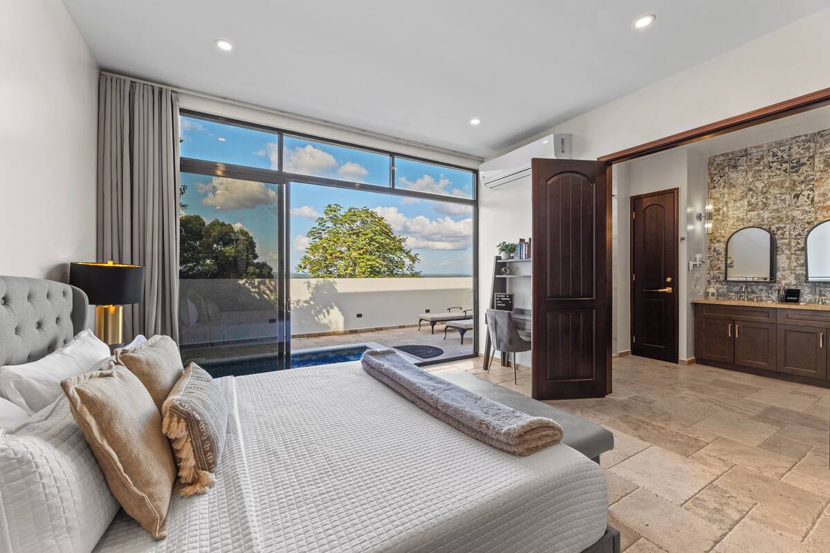 A modern bedroom with a large bed, a view of the outdoors, and a small balcony.
