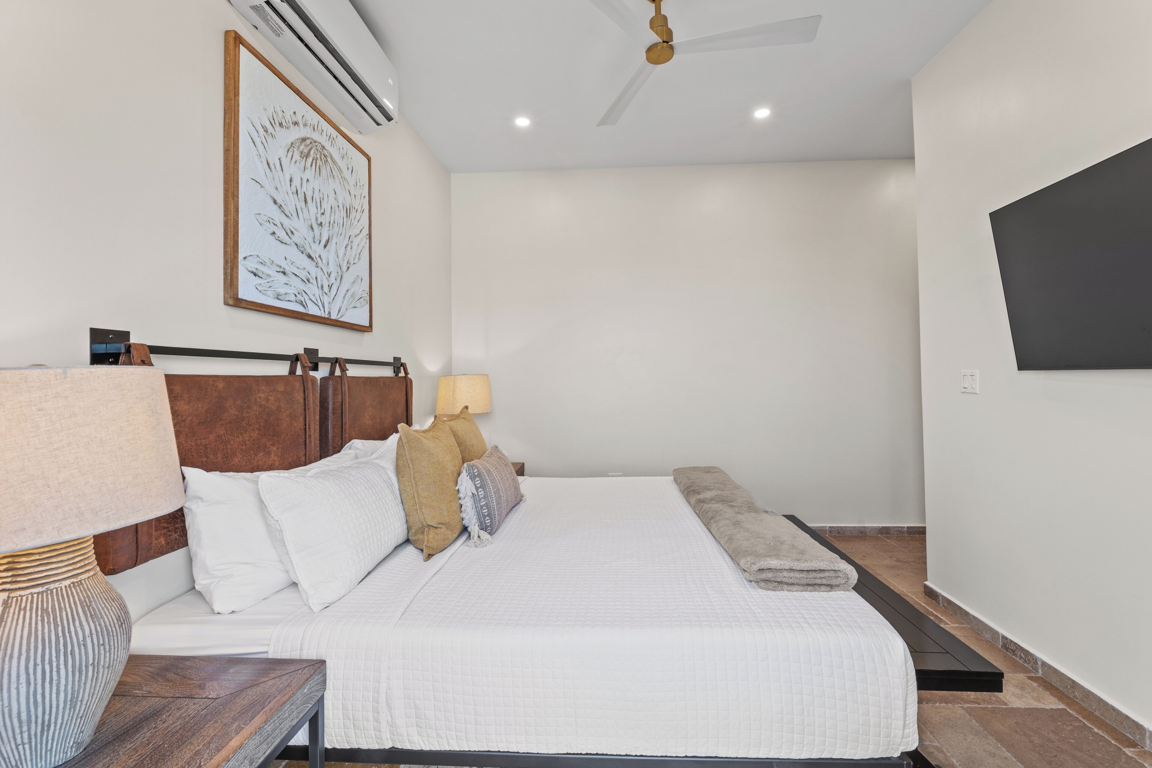 A neatly arranged bedroom with a bed, bedside table, lamp, and a wall-mounted TV.
