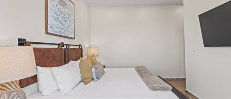A neatly arranged bedroom with a bed, bedside table, lamp, and a wall-mounted TV.