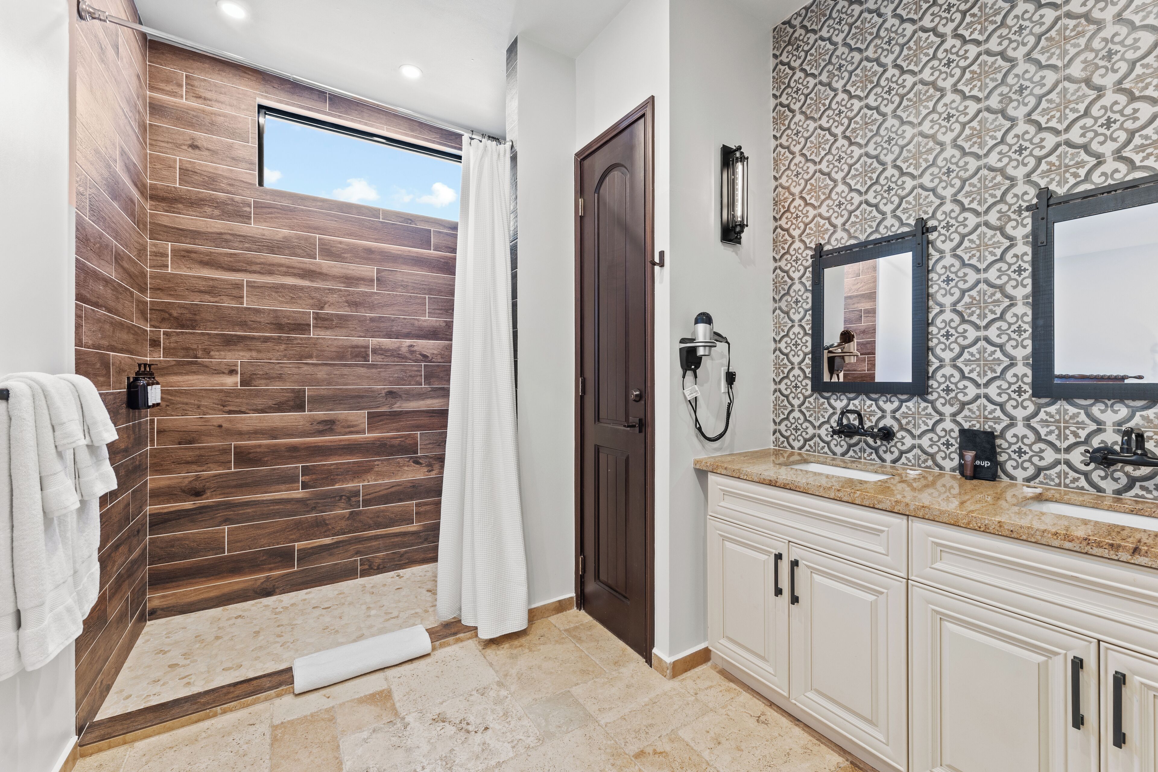 A bathroom with a wooden accent wall, a shower, a large mirror, and a vanity with a sink.