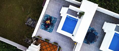 An aerial view of a modern house with a swimming pool, a patio with outdoor furniture, and a garden area.