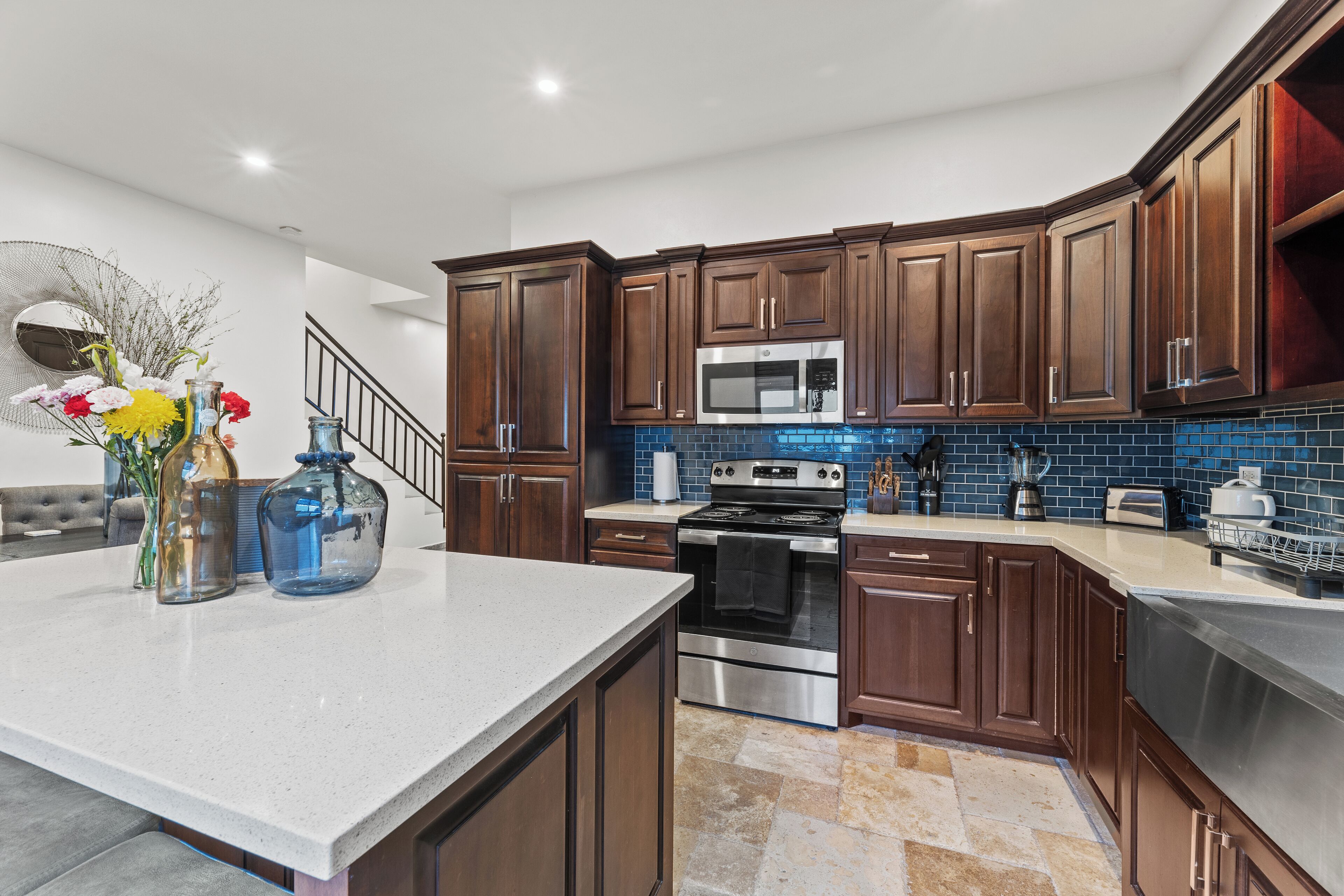 A modern kitchen with dark wooden cabinets, stainless steel appliances, and a blue-tiled backsplash.