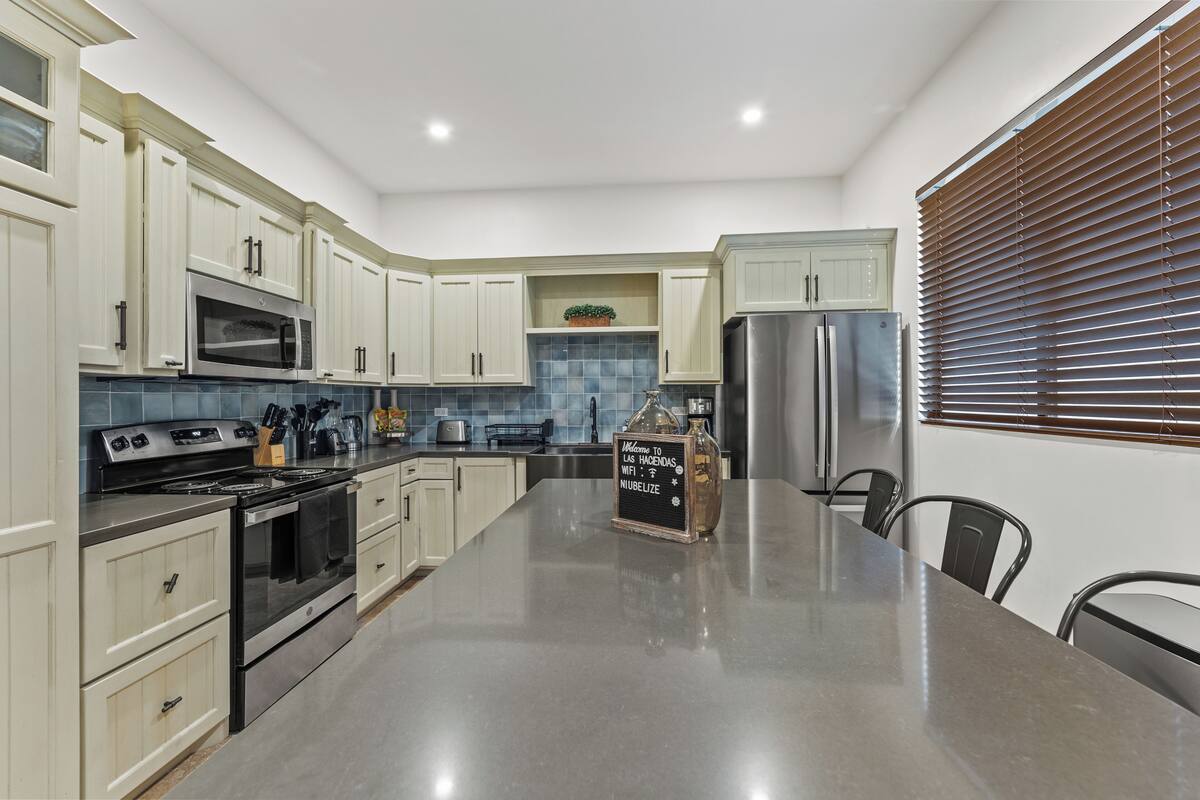 A modern kitchen with white cabinets, stainless steel appliances, a granite countertop, and a chalkboard sign.