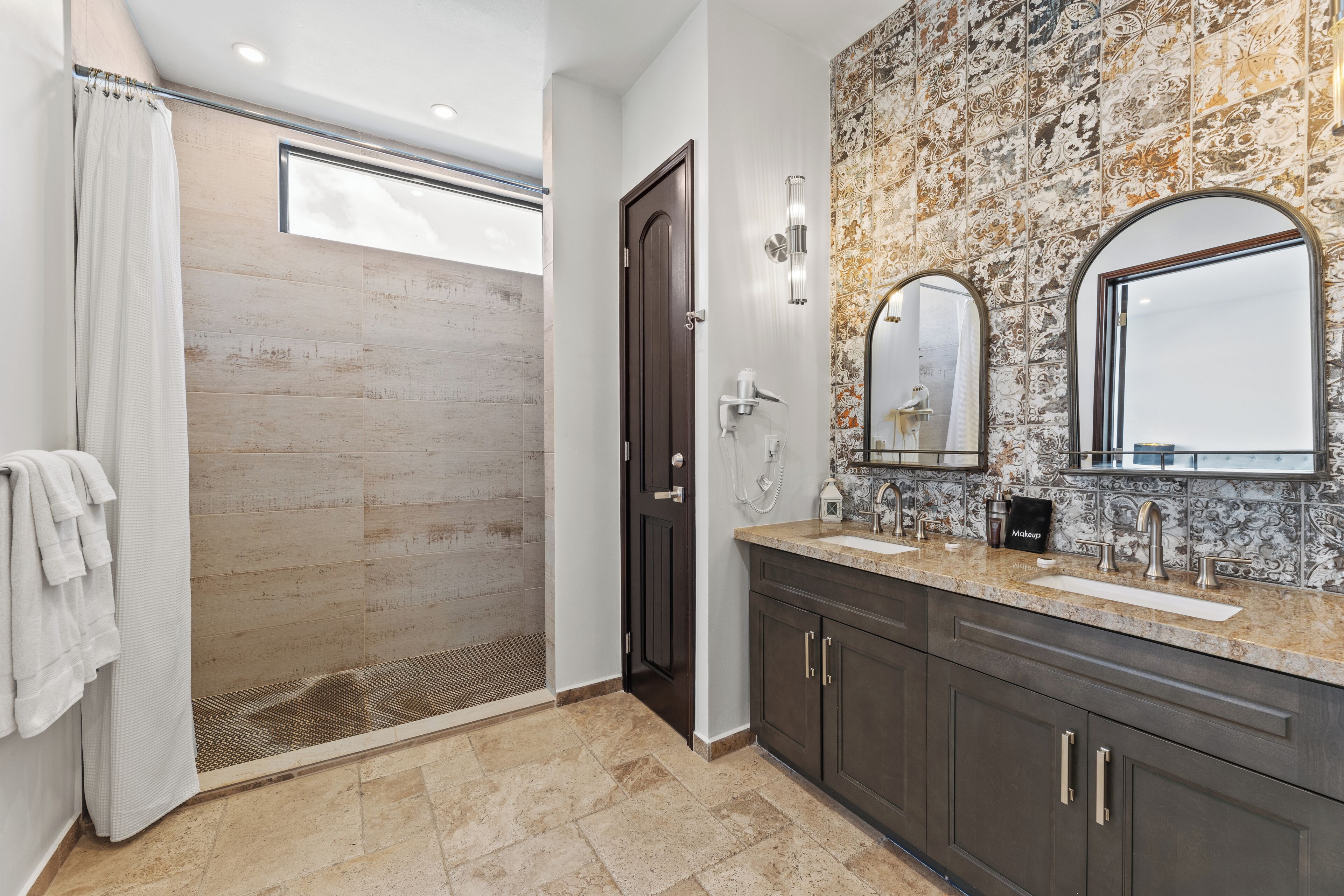 A modern bathroom with a walk-in shower, a large vanity with dual sinks, and a decorative tiled backsplash.