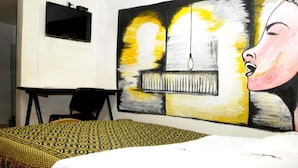 A bedroom with a bed, a desk, and a large abstract painting on the wall. - Hostal Chorro De Quevedo Candelaria (Bogotá)