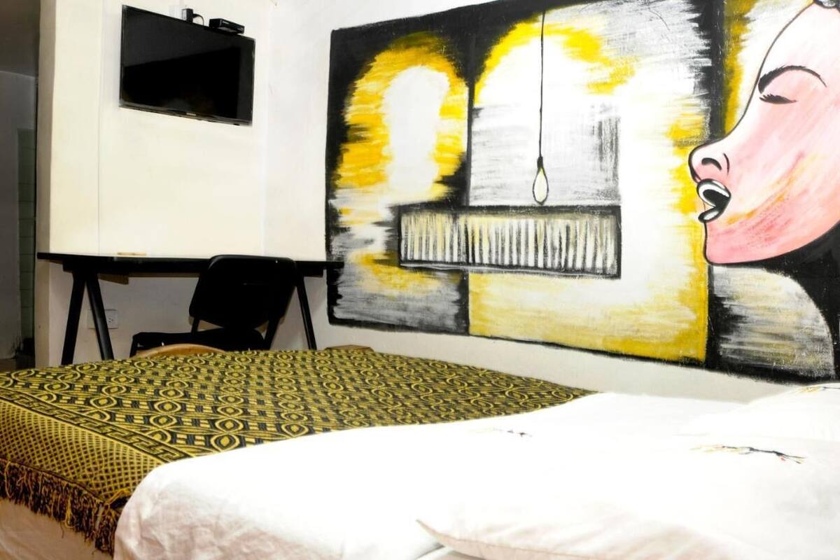 Ein Schlafzimmer mit Bett, Schreibtisch und einem großen abstrakten Gemälde an der Wand.