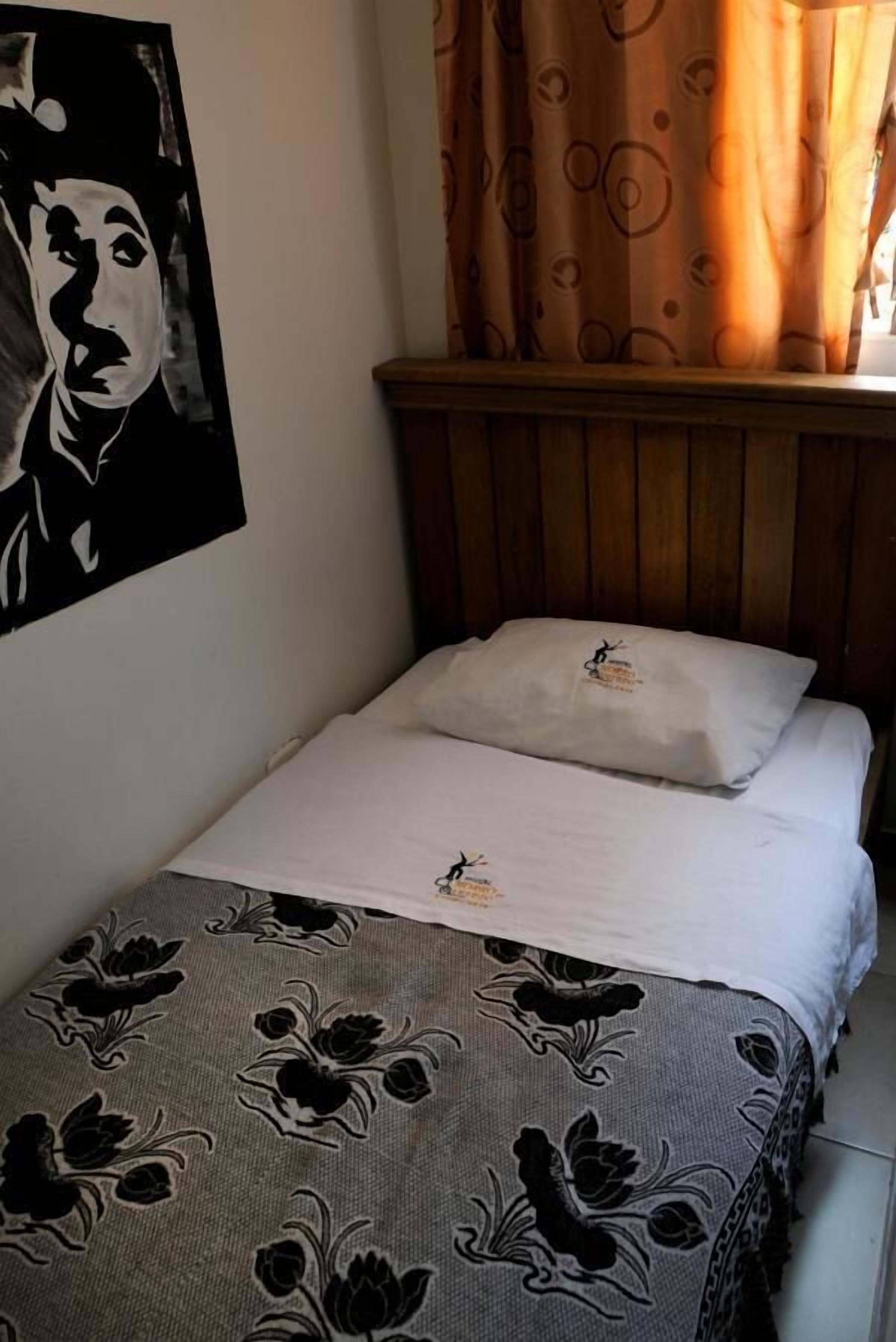 A single bed with a floral-patterned bedspread, a white pillow, and a wooden headboard.