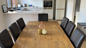 A dining area with a wooden table and black chairs, a kitchen in the background, and a framed picture on the table. - LUXURY 4 BEDROOM KING BED SPA ARCADE WIFI NETFLIX SLEEPS 10 WITH BOAT PARKING (Portland)